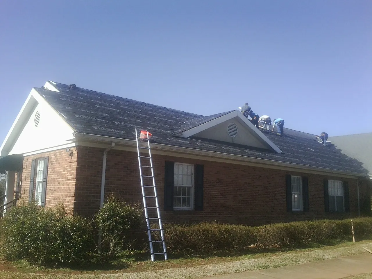 Crew tearing shingles off a brick ranch roof with a ladder set — Metal Roof Repair work by our crew in Rosburg