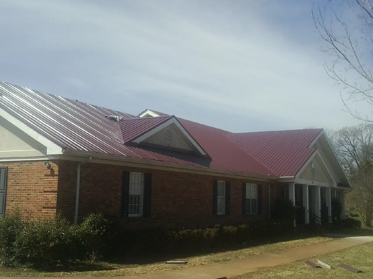 Red metal roof with gabled entries on a long brick building, from a Hail Damage Roof Repair job in Rosburg