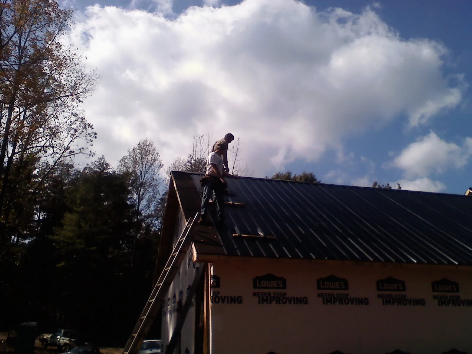 Roofer fastening dark metal panels high against a cloudy sky, from a Roof Inspection job in Rosburg