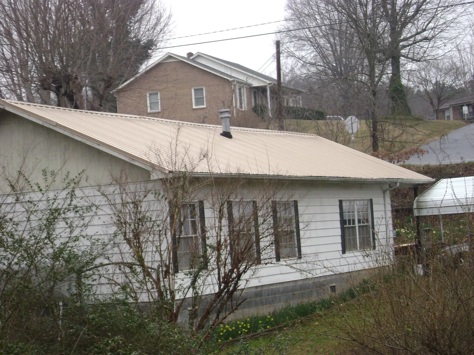 Tan metal roof on a white sided house set into a hillside — Commercial Roofing by Roofing Brothers in Rosburg